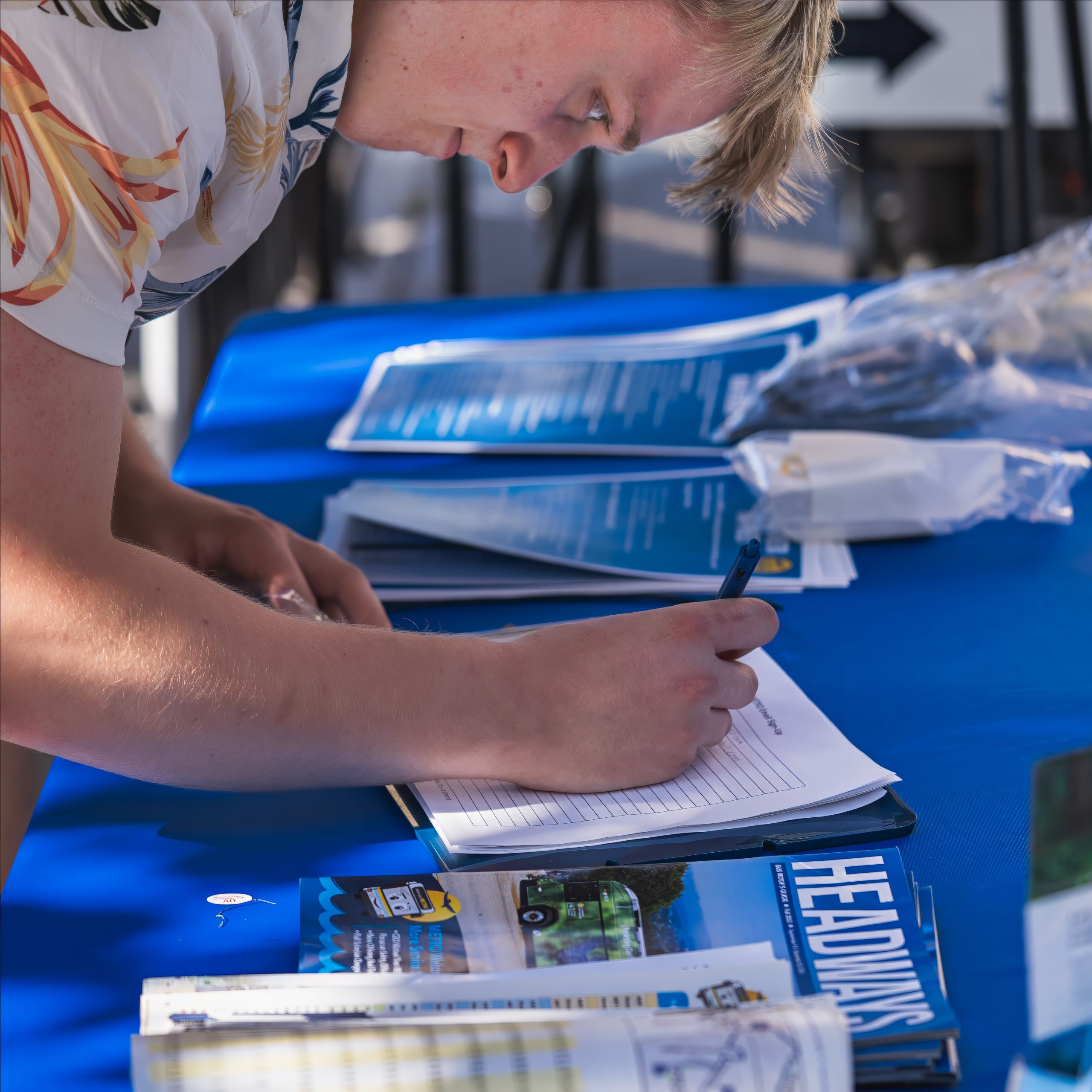 male leaning over table writing on paper