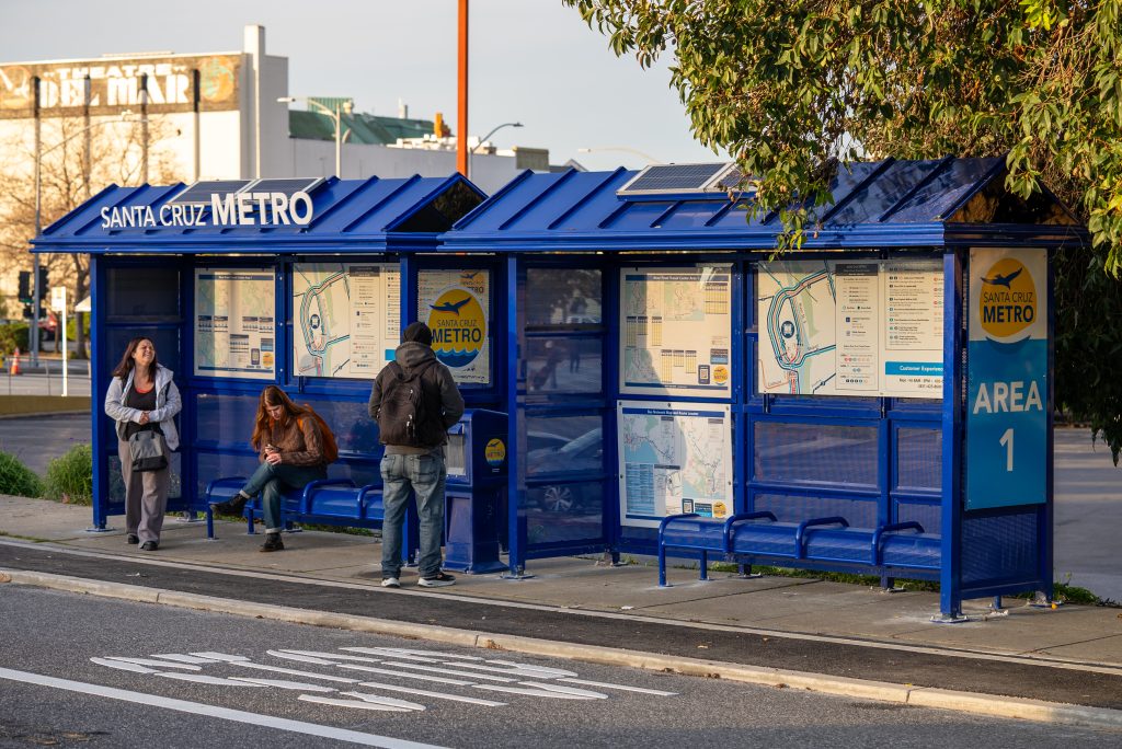 People standing waiting for bus under Santa Cruz METRO bus stop Area 1